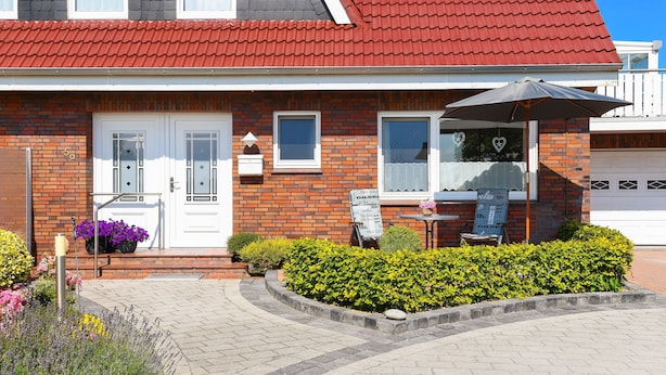 Ein zweistöckiges Haus mit rotem Dach, einer Ziegel-Fassade und einer Veranda mit Tisch und Sonnenschirm.