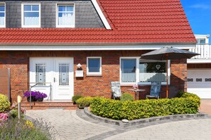 A two-story house with a red roof, a brick facade, and a front porch with a table and umbrella. - Ferienwohnung Mühlenblick im Landhaus am Grafthof - Ferienwohnung Mühlenblick (Neuharlingersiel)