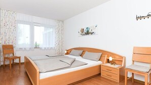 Ein Schlafzimmer mit einem hölzernen Bett, Nachttischen, einem Stuhl und einem Fenster mit Vorhängen.