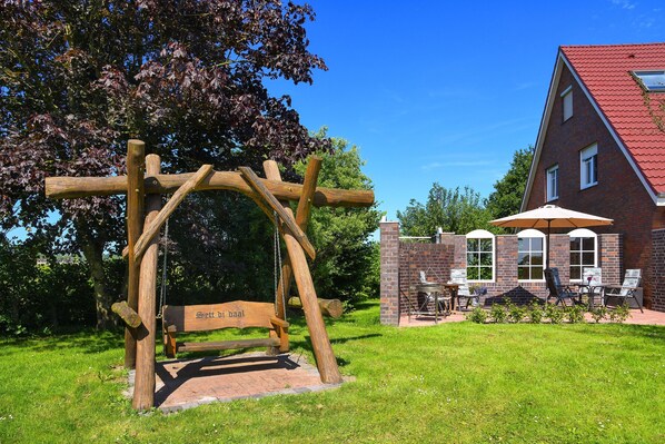 A wooden pergola with a bench, a brick building with a red roof, and outdoor seating.