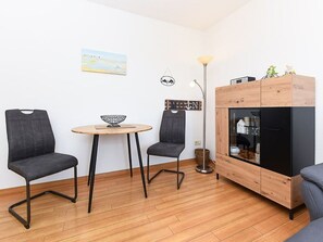A small room with two chairs, a round table, a cabinet with a television, and a painting on the wall.