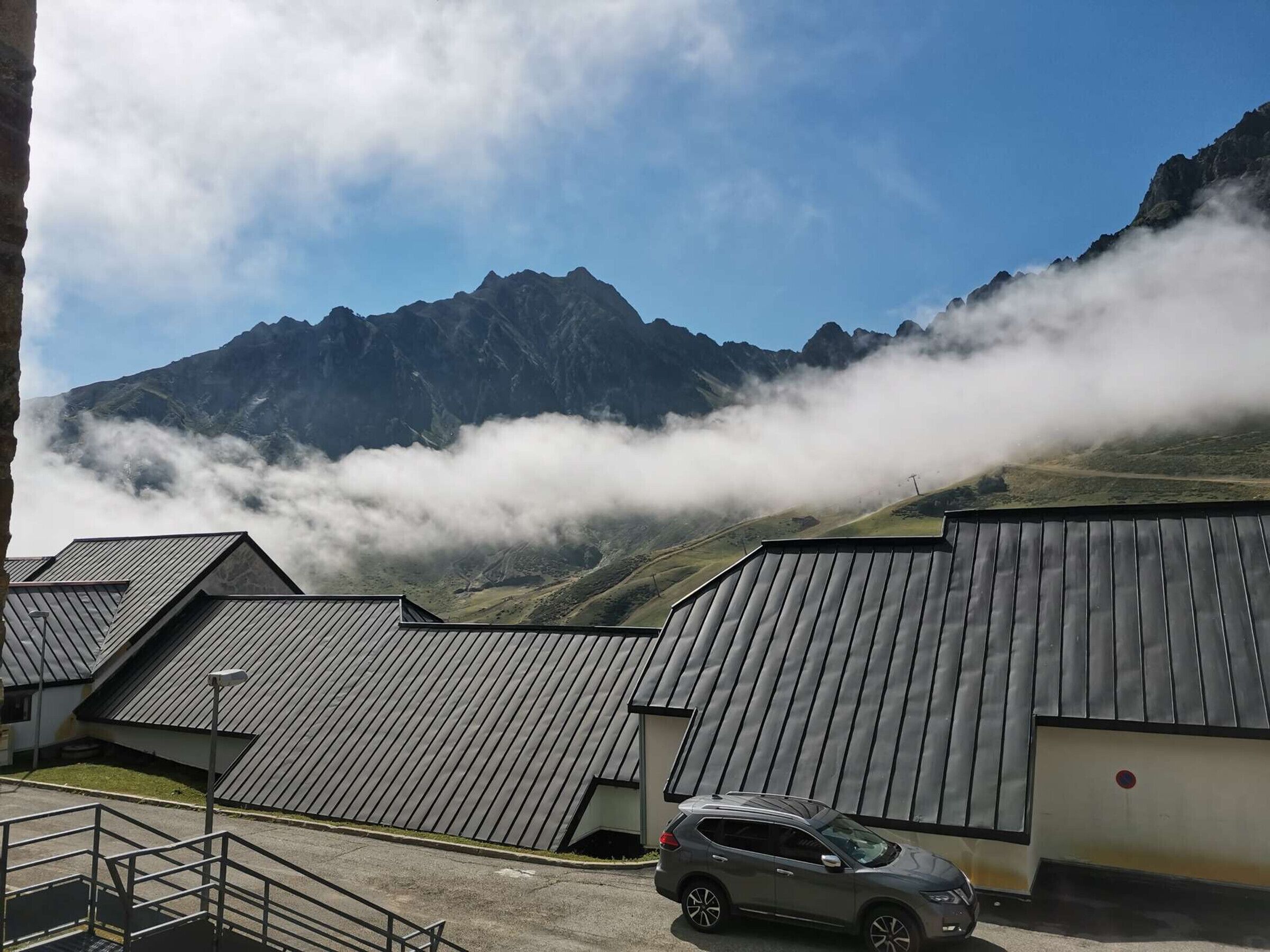 Vista de la montaña con un coche estacionado frente a un edificio de techo inclinado.