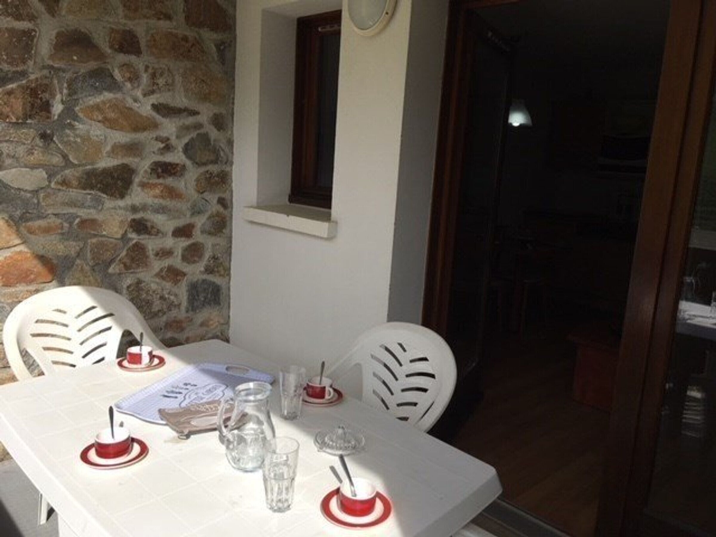A dining area with a stone wall, a small window, and a table set for two with chairs.