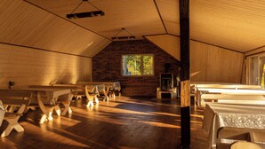 A rustic wooden interior with benches, a fireplace, and a large window.