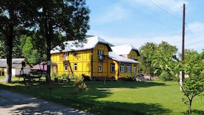 A yellow building with a sloped roof, surrounded by a green lawn and trees.