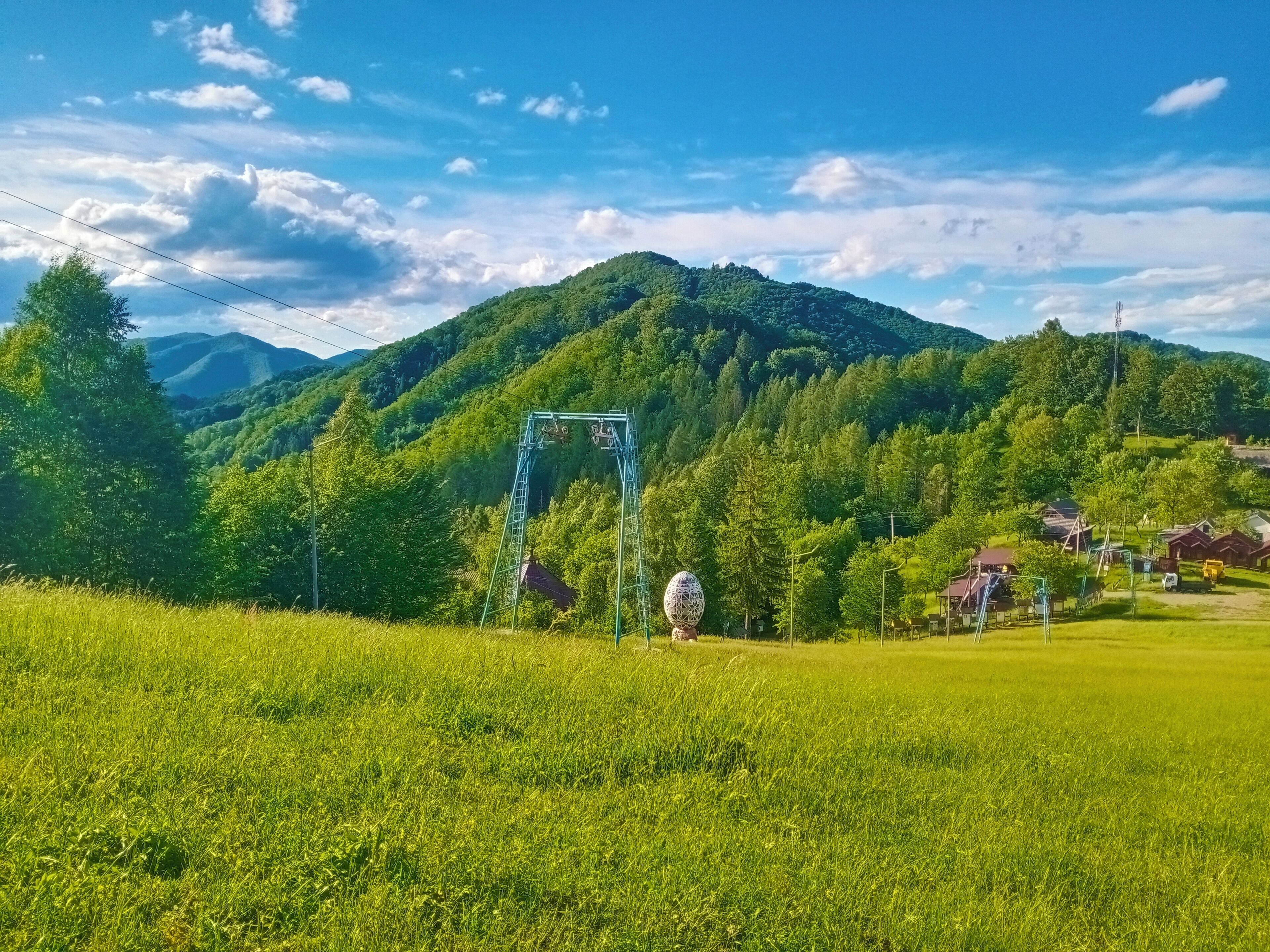 Un paysage rural avec un champ verdoyant, une structure bleue d’utilité publique et une montagne en arrière-plan.