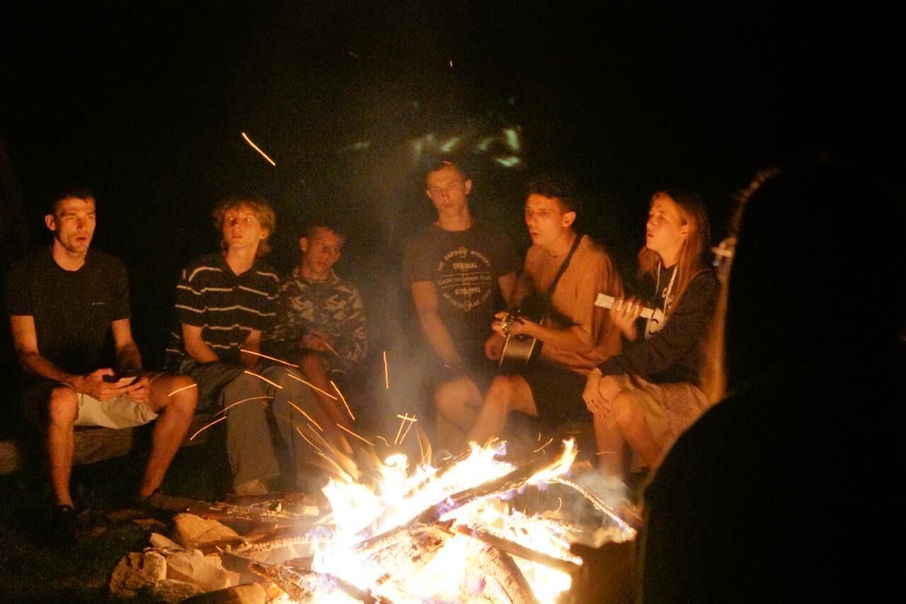 A group of people sitting around a campfire at night.