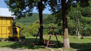 A yellow building with a hipped roof, surrounded by a grassy area with a swing set and a wooden bench.