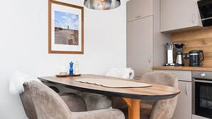 Een moderne keuken met een eettafel, stoelen, een koffiezetapparaat en een lijst aan de muur.