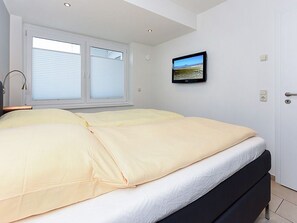 Una camera da letto con un letto, una finestra con persiane, una TV a parete e una porta.