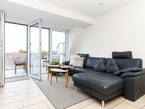 En moderne stue med en sort lædersofa, et lille rundt bord og en glasdør til en udendørs balkon.