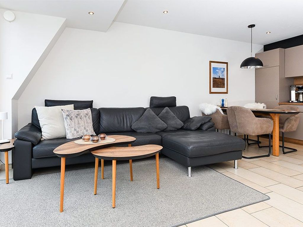 Ein modernes Wohnzimmer mit einem Ecksofa, zwei Holztischen und einem Essbereich mit Tisch und Stühlen.