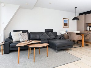 En moderne stue med en krogsofa, to træ sofaborde og et spiseområde med bord og stole.