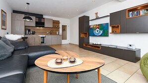 Een moderne woonkamer met een zwarte leren bank, een houten salontafel en een flatscreen televisie aan de muur.