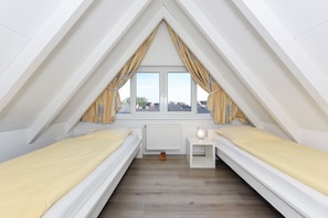 Een kleine, driekantige slaapkamer onder het dak, met twee eenpersoonsbedden, een nachtkastje en een radiator.