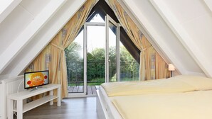 Une chambre à coucher avec un lit, un téléviseur posé sur un meuble et un balcon avec des rideaux.