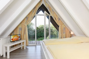 Een slaapkamer met een bed, een televisie op een standaard en een balkon met gordijnen.