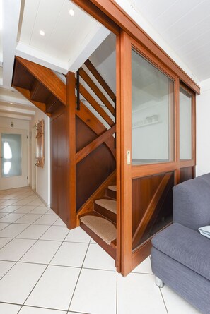 A modern interior with a wooden staircase, a grey sofa, and a tiled floor.