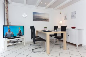 A modern, well-lit room with a dining table, chairs, a television, and a cabinet.