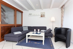 Een moderne woonkamer met een grijze bank, een witte salontafel, een zwarte fauteuil en een blauw vloerkleed.