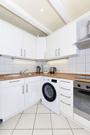 A modern kitchen with white cabinets, a built-in washing machine, and a stainless steel range hood.