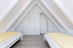 A bedroom with a sloped ceiling, two beds with yellow bedding, and a white wardrobe.