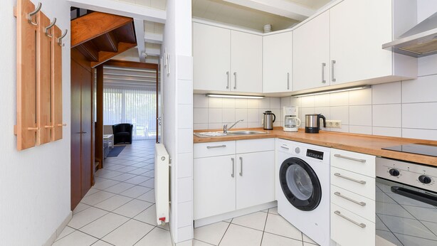 Une cuisine moderne avec des meubles blancs, un lave-linge et une machine à café.