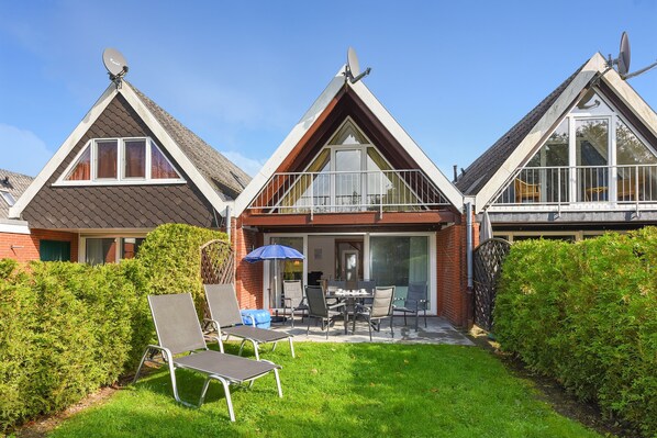 A two-story house with a balcony, a patio with outdoor furniture, and a well-maintained garden.