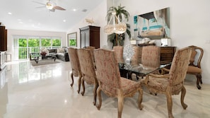 A spacious dining area with a glass table surrounded by ornate chairs, a ceiling fan, and a large painting of a beach scene. - 801 Mariners Club - Luxury Key Largo Townhouse (Key Largo)