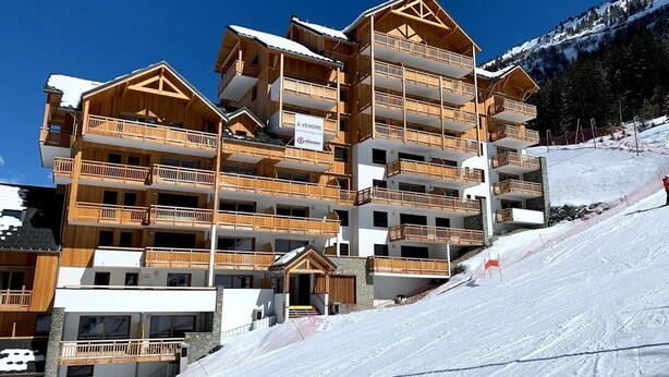 Un hotel de estilo chalé con varios pisos y balcones, ubicado en una ladera nevada bajo un cielo despejado.