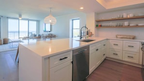 A modern kitchen with white cabinetry, a central island, and a pendant light. - Enjoy Modern Luxury Design in this Oceanfront, Corner Unit!  Stunning Ocean Views & Community Pool. (Folly Beach)