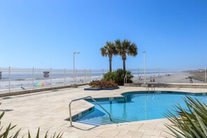 A pool area with a clear view of the beach and ocean.