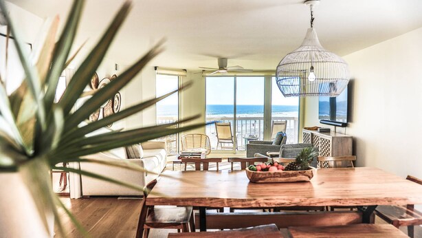 A dining area with a wooden table, chairs, a ceiling fan, and a view of the ocean. - Enjoy Modern Luxury Design in this Oceanfront, Corner Unit!  Stunning Ocean Views & Community Pool. (Folly Beach)
