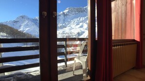 Une pièce avec vue sur des montagnes enneigées, un plancher en bois et un rideau rouge.