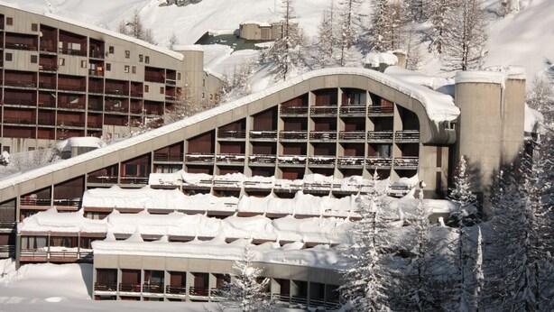 Un hôtel à plusieurs étages, doté de balcons, avec une piste de ski en arrière-plan.