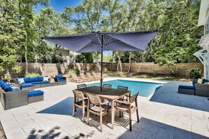 Un jardin avec une piscine, du mobilier d’extérieur et un grand parasol.