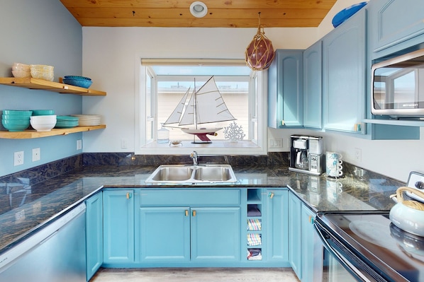 Una cocina moderna con armarios azules, techo de madera, ventana decorada con un velero y una cafetera.