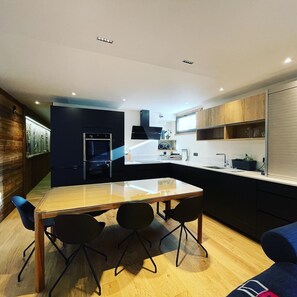 Une cuisine moderne dotée d’un îlot central, de meubles de couleur noire et d’une table à manger en bois, accompagnée de quatre chaises.