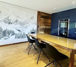 Une cuisine moderne avec une table et des chaises en bois, une grande fresque représentant un paysage de montagne enneigé et un four encastré.