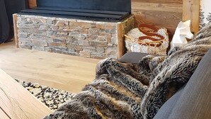 A modern living room with a stone fireplace, wooden panel walls, a flat-screen TV, and a cozy seating area. - 80 m2, ski in / out center Alpe d'huez, luxury 8p 3bdrm 3bathroom 3 terraces with fireplace SPOT (ALPE D HUEZ)