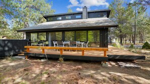 A modern cabin with a covered deck, outdoor seating, and a view of the surrounding forest. - 1 Crag-Sunriver, Oregon: Hot Tub, Pet Friendly, BBQ, WiFi, SHARC Aquatics, Tubing Hill, Mt. Bachelor, Golf, Deschutes River, Tennis, Bike Paths (Sunriver)