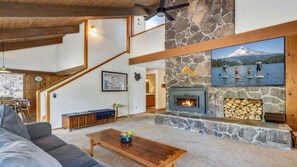 A cozy living room with a stone fireplace, a staircase, and a dining area.