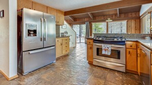 A kitchen with a stainless steel refrigerator, a gas stove, wooden cabinets, and a stone tile floor. - 1 Crag-Sunriver, Oregon: Hot Tub, Pet Friendly, BBQ, WiFi, SHARC Aquatics, Tubing Hill, Mt. Bachelor, Golf, Deschutes River, Tennis, Bike Paths (Sunriver)
