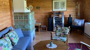 A cozy cabin interior with a blue sofa, a wooden coffee table, cactus-patterned chairs, a patterned rug, and a wooden ceiling. - Ferienhaus mit Kachelofen (Grafenau)