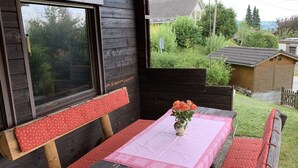 A wooden deck with a picnic table and benches, surrounded by a wooden cabin and a garden. - Ferienhaus mit Kachelofen (Grafenau)
