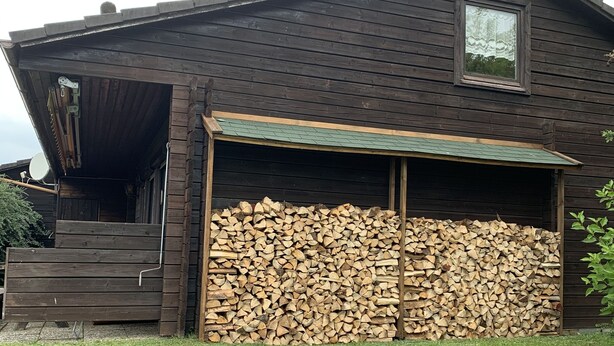 A wooden house with a garage door, a stack of firewood, and a satellite dish. - Ferienhaus mit Kachelofen (Grafenau)