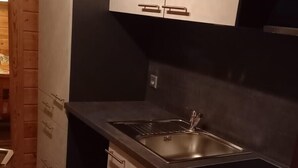 A compact kitchen with wooden cabinets, a stainless steel sink, and an oven. - Ferienhaus mit Kachelofen (Grafenau)