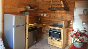 A compact kitchen with a refrigerator, oven, and sink, wooden walls, and a chandelier.