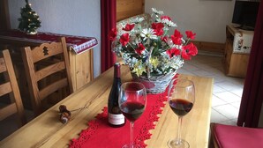 A dining table with a bottle of red wine, two glasses of red wine, and a floral centerpiece.