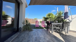 Un patio al aire libre con una mesa y sillas, una pérgola que da sombra y plantas en macetas.